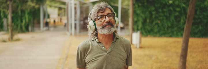 Friendly middle-aged man with gray hair and beard wearing casual clothes listening to music on...
