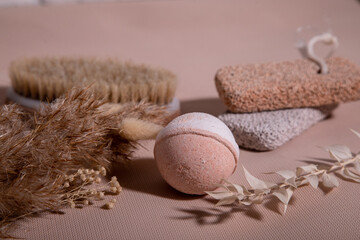 a peach bath bomb lies against the backdrop of leg pumice, dry body masage brush and dry flowers.