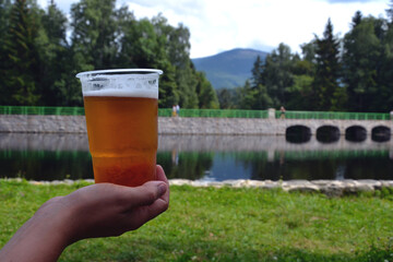 Karpacz, Poland. Cold beer in plastic cup with the Wild Waterfall (polish: Dziki Wodospad) – an...