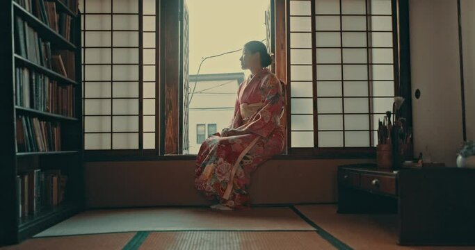 Thinking, morning and traditional Japanese woman by window for reflection, calm and wellness. Kimono, culture and happy person in home with view for thoughtful, wondering and relaxing in living room