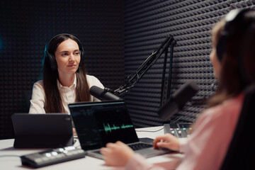 A woman host and her guest, deep in conversation during a podcast, indoors, showcasing...