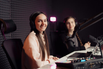 Two female podcasters, one with a radiant smile, in a soundproof studio, displaying confidence and ease during a live podcast recording session