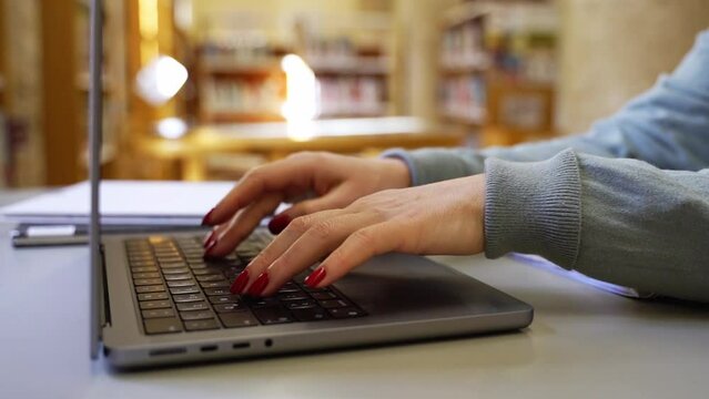 Close-up woman hands typing on keyboard using laptop in public place, coworking. Business or freelancer working remotely. Adult student studying in public library Technology in education and business