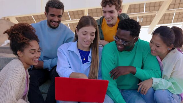 Young group of multiracial students working together on laptop sitting outdoors at college campus. Millennial friends discussing about university assignment or project. Education and teamwork.