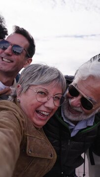 Vertical group diverse funny middle-aged tourist friends posing laughing taking photo selfie embracing together with front camera on travel outdoor. Mature happy six people enjoy holidays sunny day 