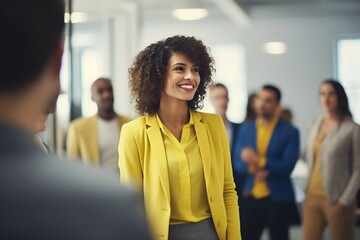 Obraz premium A radiant woman in yellow with a blurred team in the backdrop, in a bright corporate setting