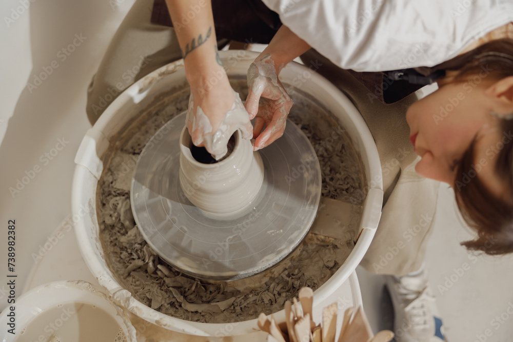 Wall mural close up of hands of professional potter molding pot shape on pottery wheel. ceramics art concept