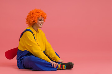funny clown in a wig and a yellow-blue suit with a propeller on his back sits on a colored...