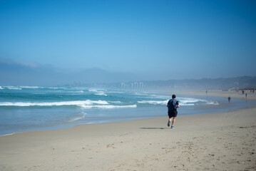 a man with a blue shirt running on the sand during a sunny day