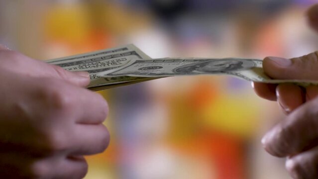 Person's hands hold money and pass it to another person's hands one dollar bill at a time. Scam, blackmailing, debt collectors concept