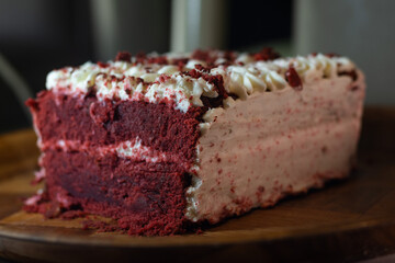Horizontal photograph without people of a slice of red velvet cake decorated with cream, inside a kitchen on a wooden tray