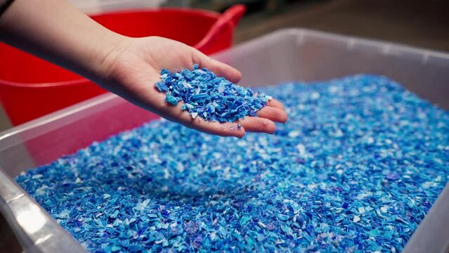 Close-up of shredded plastic lids stored in a special container at a waste recycling station hand holding the product