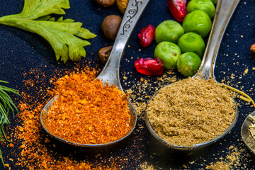 Spices and ground coriander lie on two teaspoons close-up on a dark background next to green peas...