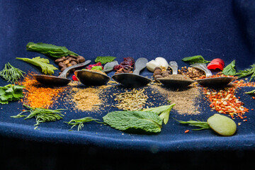 spices scattered in front of five teaspoons around greenery on a black background	
