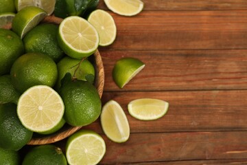 Fresh wet whole and cut limes on wooden table, flat lay. Space for text