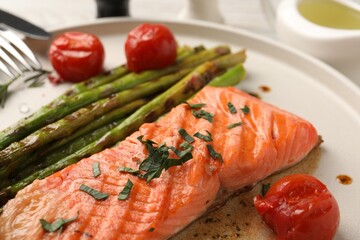 Tasty grilled salmon with tomatoes, asparagus and spices on table, closeup