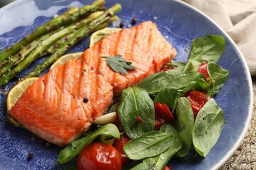 Tasty grilled salmon with tomatoes, asparagus, spinach and spices on plate, closeup