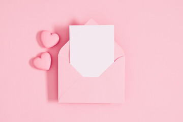 Open pink envelope with paper card and heart on pastel pink table background. Birthday, Wedding, Mother's Day, Valentine's day, Women's Day. Flat lay, top view, copy space