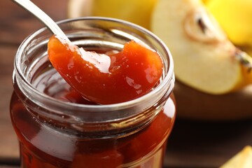 Taking tasty homemade quince jam from jar at table, closeup