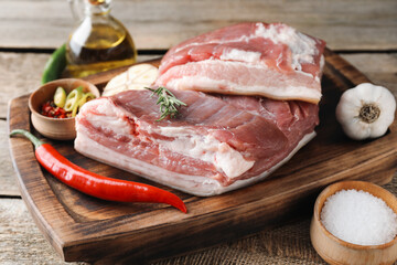 Pieces of raw pork belly, chili pepper, oil, garlic and rosemary on wooden table
