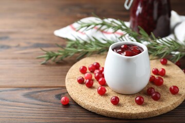 Fototapeta na wymiar Cranberry sauce in pitcher fresh berries and rosemary on wooden table, closeup. Space for text