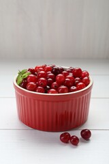 Fresh ripe cranberries in bowl on white wooden table, closeup