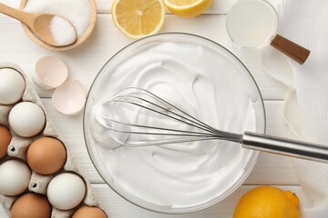 Bowl with whipped cream, whisk and ingredients on white wooden table, flat lay