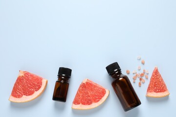 Grapefruit essential oil in bottles, sea salt and cut fruit on light blue table, flat lay. Space...
