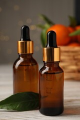 Bottles of tangerine essential oil and green leaf on white wooden table, closeup