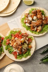 Delicious tacos with vegetables and meat on grey textured table, flat lay