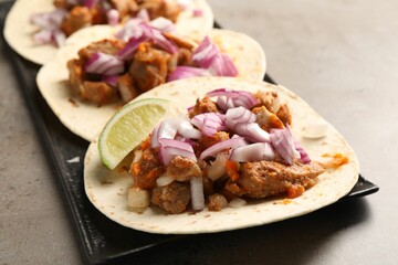 Delicious tacos with vegetables, meat and lime on grey textured table, closeup