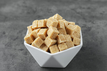 Brown sugar cubes in bowl on grey table