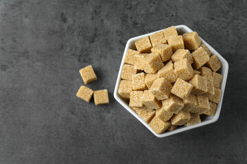 Brown sugar cubes in bowl on grey table, top view. Space for text