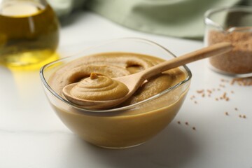Spoon and glass bowl with tasty mustard sauce on white table, closeup
