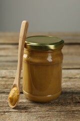 Jar and spoon with tasty mustard sauce on wooden table, closeup