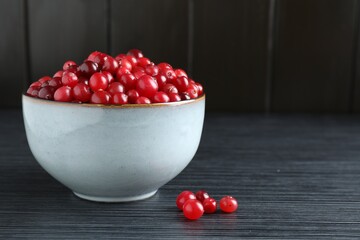 Cranberries in bowl on black wooden table, closeup. Space for text