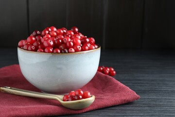 Cranberries in bowl and spoon on black wooden table, closeup. Space for text