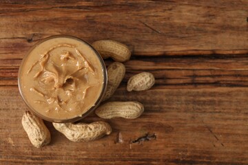 Delicious nut butter in bowl and peanuts on wooden table, top view. Space for text