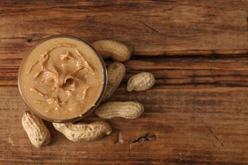 Fototapeta premium Delicious nut butter in bowl and peanuts on wooden table, top view. Space for text