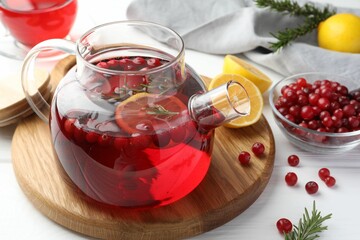 Tasty hot cranberry tea with lemon, rosemary and fresh berries in teapot on white wooden table