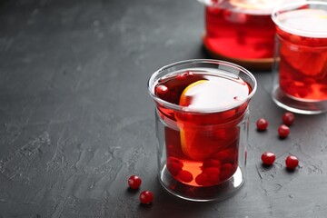 Tasty hot cranberry tea with lemon and fresh berries in glass on black textured table