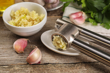 Garlic press, cloves and mince on wooden table, closeup
