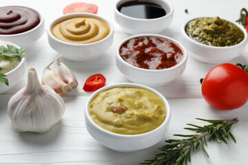 Many different sauces, spices and vegetables on white wooden table
