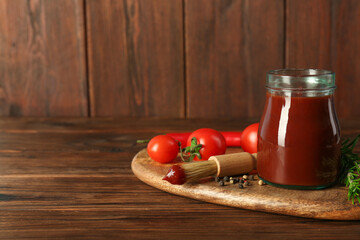 Tasty barbecue sauce in glass jar, brush and ingredients on wooden table, closeup. Space for text