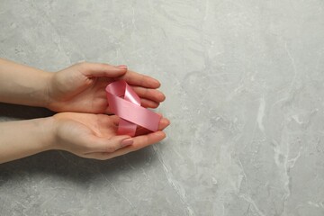 Breast cancer awareness. Woman with pink ribbon at grey marble table, top view. Space for text