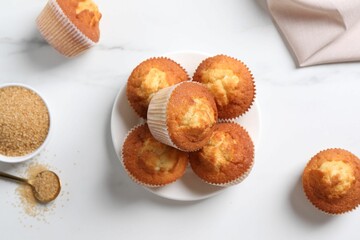 Delicious sweet muffins and brown sugar on white marble table, flat lay