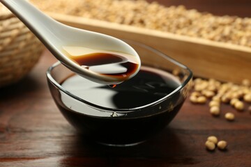 Taking soy sauce with spoon from bowl at wooden table, closeup