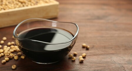 Soy sauce in bowl and soybeans on wooden table, closeup. Space for text