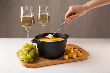 Woman dipping piece of bread into fondue pot with tasty melted cheese at white table, closeup