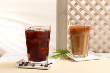 Refreshing iced coffee with milk in glasses and beans on beige table